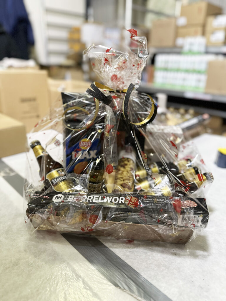 In cellofaan verpakt geschenkpakket met wijnflessen en lekkernijen