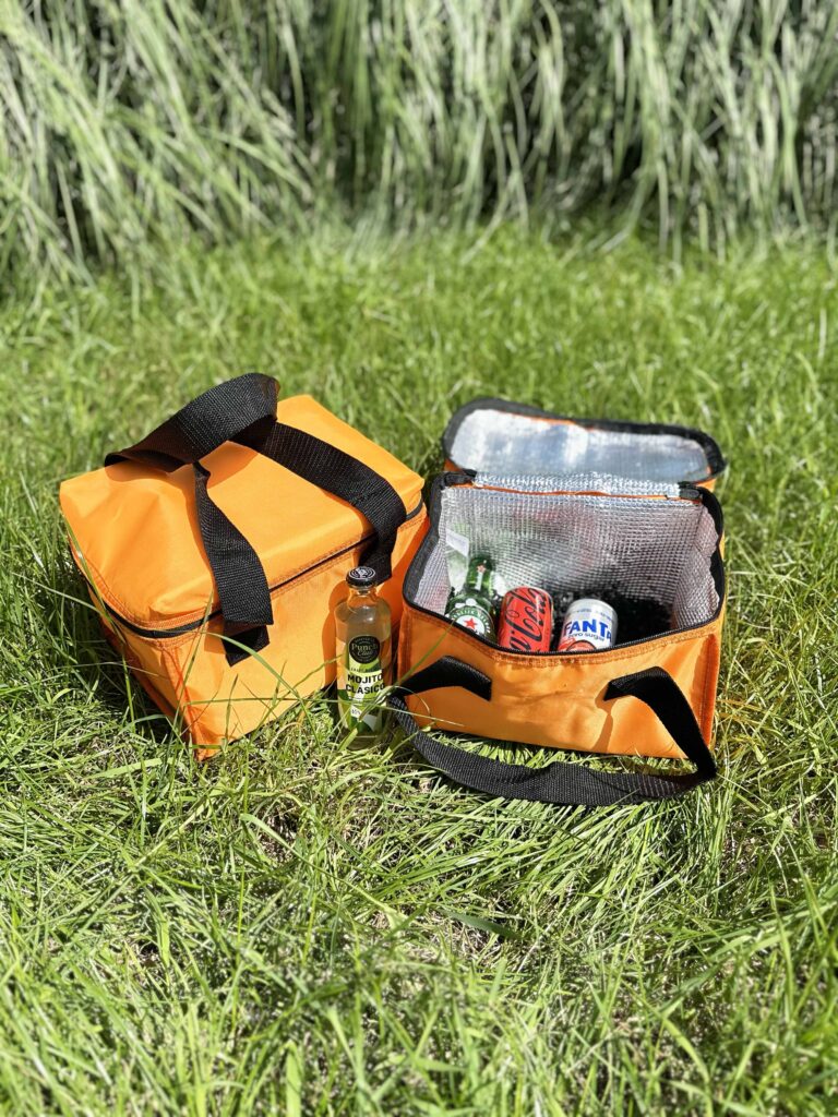 Oranje koeltas gevuld met drankjes, geopend in het gras